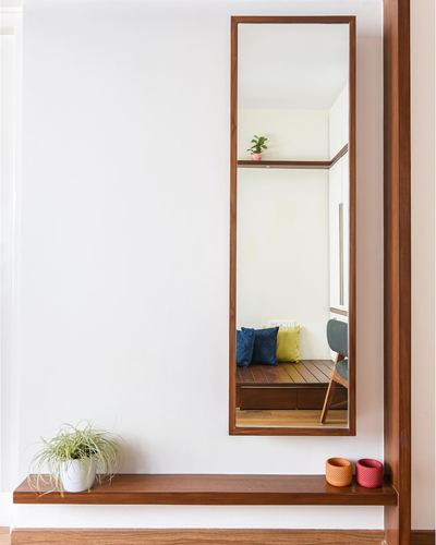 Tall wooden-framed mirror above a slim console shelf reflecting a seating nook