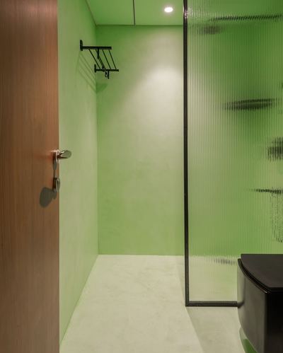 Green plaster bathroom with wooden door, black towel rack, and fluted glass shower partition