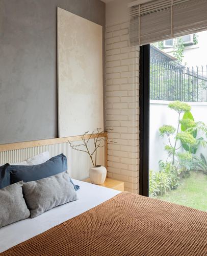 Minimalist bedroom corner with textured grey wall, brick niche, and full-height glass door to garden