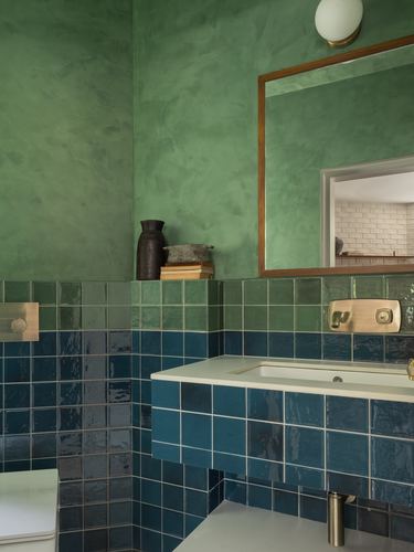 Green plastered bathroom wall above blue glazed tile with brass-framed mirror and vanity
