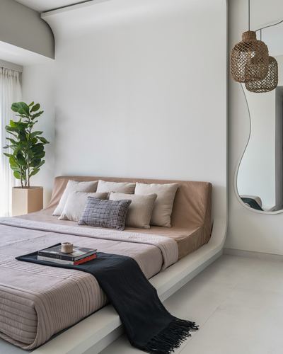 Minimalist bedroom with low upholstered platform bed, wavy mirror, and rattan pendant lights beside a potted plant.