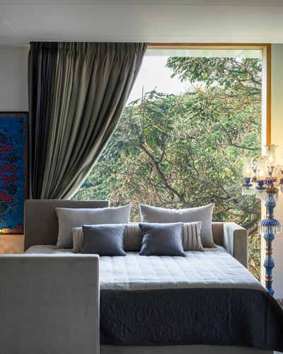 Bed with layered grey pillows facing a large window overlooking dense green trees