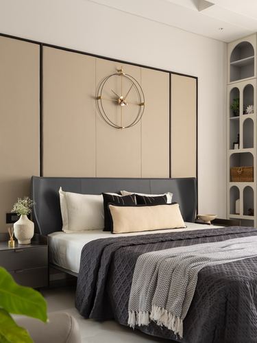 Bedroom with grey leather headboard, beige paneled wall, and large round wall clock above bed