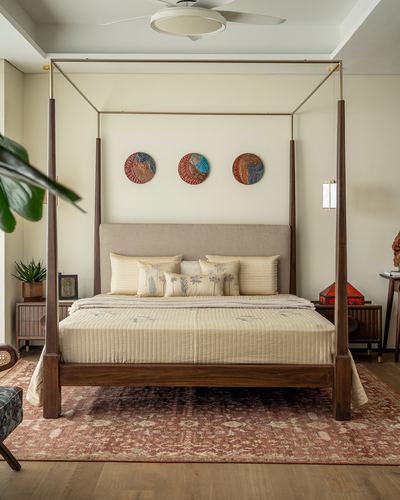 Wood and brass four-poster bed with upholstered headboard beneath three round ceramic wall discs, on a patterned rug.