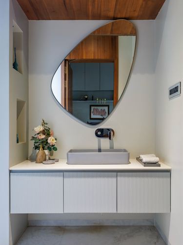 Powder room with organic mirror, vessel sink, fluted white cabinetry and wood ceiling accent