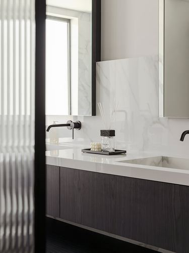 Modern bathroom vanity with marble backsplash, dark wood cabinetry, and black wall-mounted faucet.