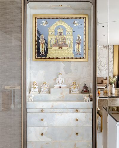 Pooja niche with gilded tirthankara painting, marble idols, and stone drawer unit below