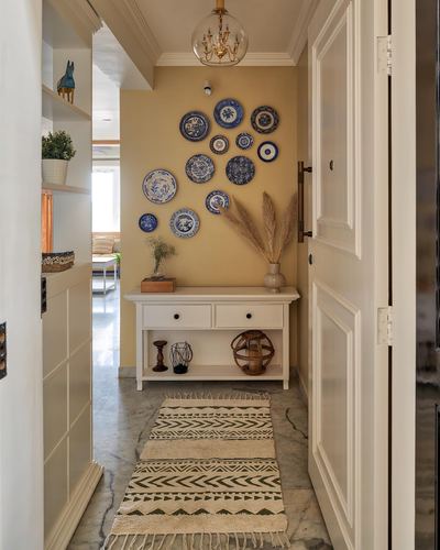 Foyer with mustard wall, blue-white plate display, white console and marble floor runner