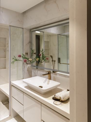 Marble-clad bathroom with vessel sink, brass faucet, arched mirror, and glass shower partition