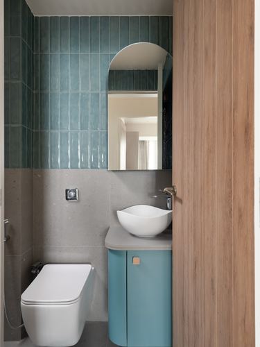 Small bathroom with teal ribbed tile, arched mirror, rounded teal vanity and wall-hung toilet