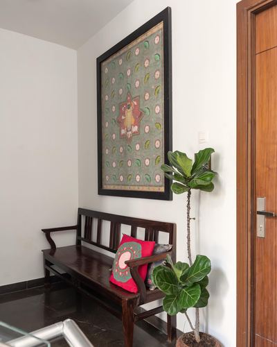 Entryway bench under framed textile art beside a fiddle leaf fig and wooden door