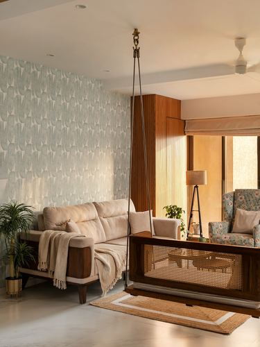 Living room with hanging cane swing, beige sofa, floral armchair and patterned green wallpaper