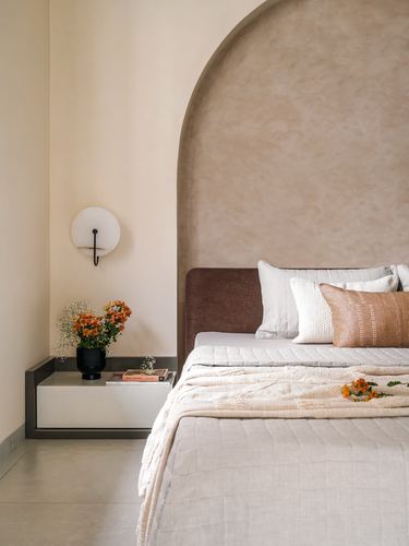 Bedroom with arched plaster alcove behind bed, round wall sconce, and nightstand with flowers