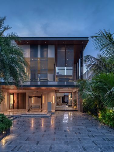 Twilight facade of a multi-storey villa with louvered screen, stone driveway, and entrance swing framed by palms