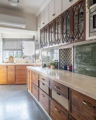 Colonial-style kitchen with arched wooden glass cabinets, green tile backsplash, and cane-front drawers on an island counter.