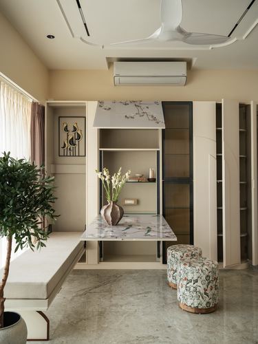 Beige study nook with fold-down marble-top desk, floral stools, and floor plant in Mumbai apartment.