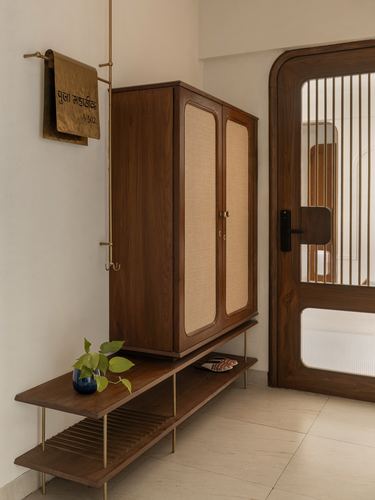 Wooden cane-front cabinet beside arched glass door in warm-toned foyer with hanging brass name plate