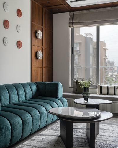 Teal channel-tufted sofa with nesting marble-top tables beside window seat and wood-panelled wall