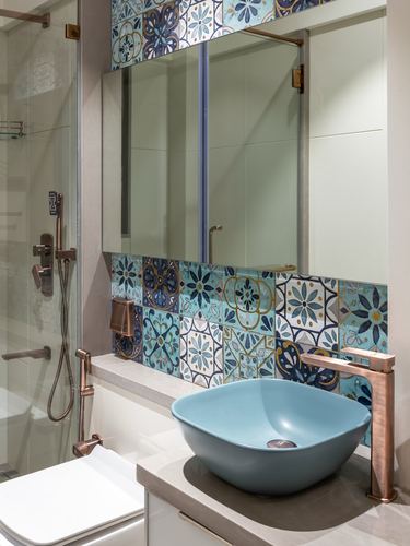 Bathroom vanity with blue vessel sink, copper faucet, and patterned tile backsplash under mirror