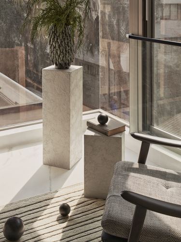 Textured plinth pedestals with plant and books beside window and armchair in sunlit corner