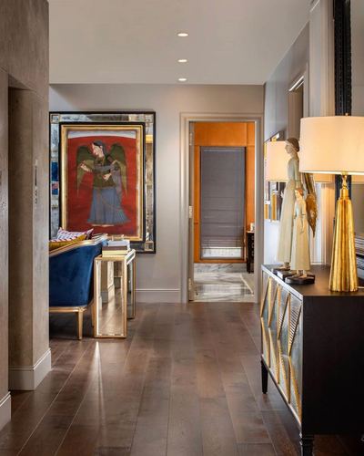 Entry hallway with framed religious artwork, mirrored console, gold lamps, and view into orange-trimmed passage.
