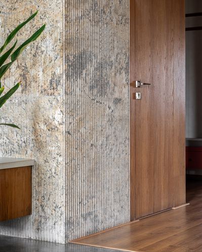 Corner detail of fluted stone wall meeting a tall wooden door with brass handle