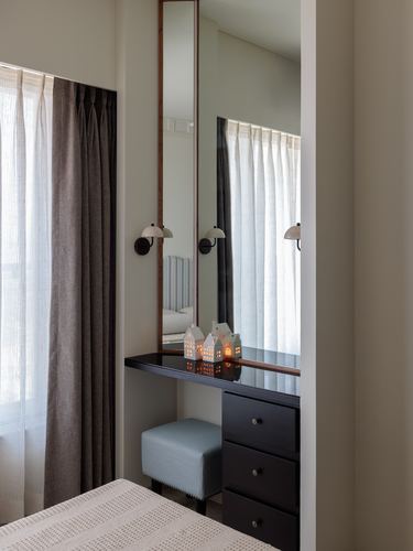 Dark wood dressing table with mirror, sconces, and blue stool by curtained window