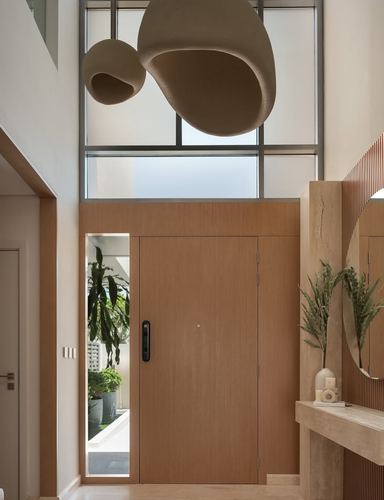 Minimalist foyer with wooden door, fluted stone console, round mirror, and sculptural pendant lights under a double-height window