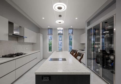 Long white galley kitchen with island, round pendant lights, and glass display cabinets