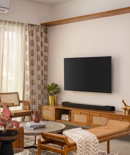Living room with teak cane-front media unit, wall-mounted tv, cane armchair and chaise, printed curtains