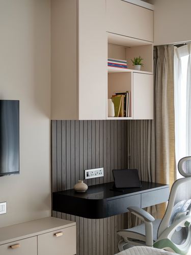 Built-in study nook with fluted wood panelling, floating black desk, and open beige shelving.