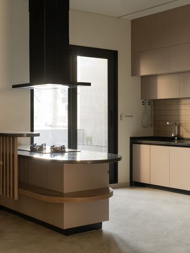 Curved wood kitchen island with black hood beside a glazed door in a beige kitchen