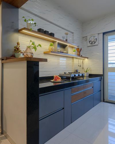 Contemporary kitchen with navy cabinetry, black stone counters, and wood floating shelves in Pune home