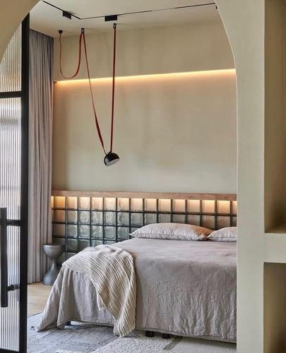 Bedroom with glass block headboard wall, arched opening, and red-corded pendant lamp
