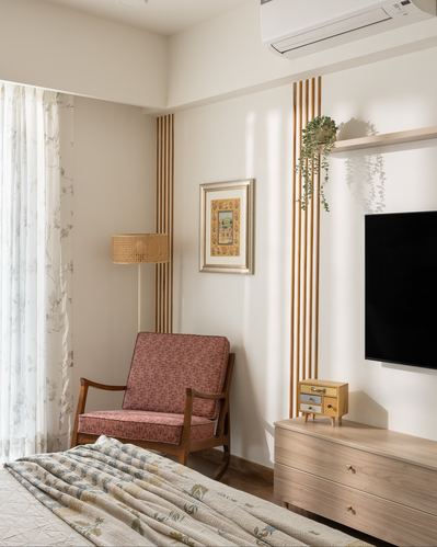 Bedroom corner with cane-shade floor lamp, pink armchair, fluted wood panel wall and wall-mounted tv above wood dresser
