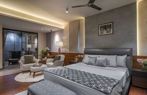 Grey upholstered bed with cove-lit walls and adjoining seating nook in master bedroom