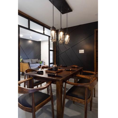 Wooden dining table with cane armchairs under three pendant lights against a black diagonal-panelled wall