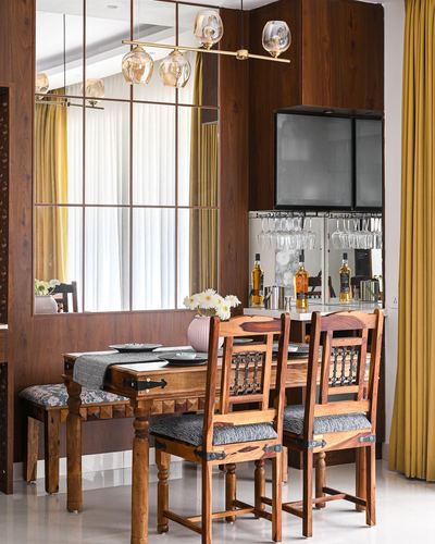 Wooden dining table with carved chairs beneath a mirrored wall and hanging bar cabinet