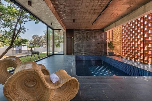 Indoor swimming pool with sculptural rattan loungers beside a glowing perforated screen wall