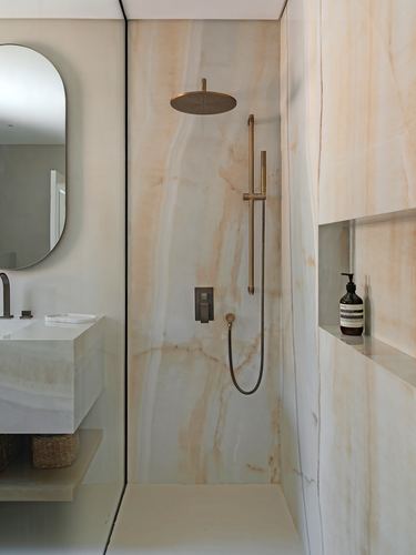 Marble-clad walk-in shower with brass fixtures and a recessed stone niche in a Dubai villa bathroom