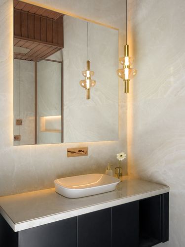 Backlit mirror above vessel sink with brass pendant lights in a stone-clad powder room