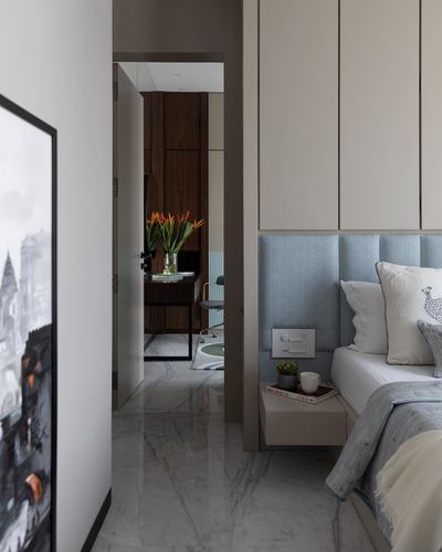 Bedroom with blue tufted headboard and floating nightstand, view through door to study with marble flooring