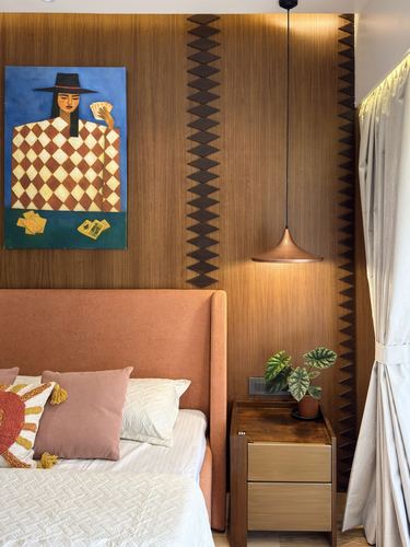 Bedroom corner with terracotta headboard, patterned wood panelling, copper pendant, and figurative artwork