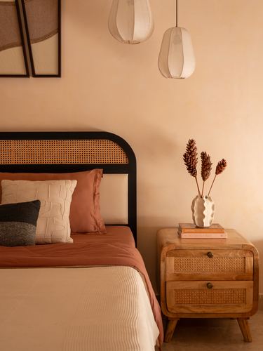 Cane headboard bed with terracotta linens beside wooden cane nightstand and paper pendant lamps