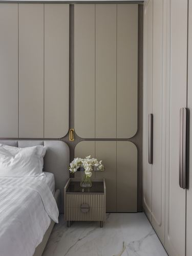 Beige panelled wardrobe wall beside bed with small nightstand and flowers on marble floor