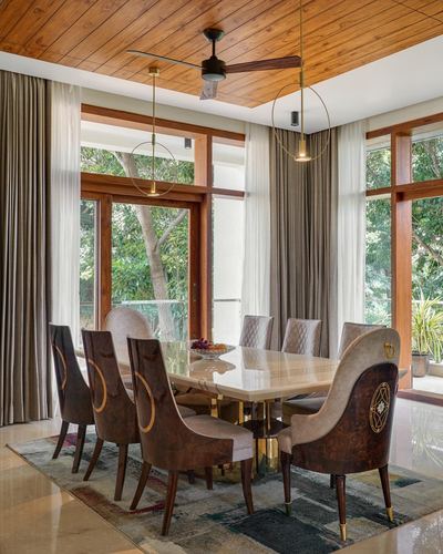 Dining room with marble table, mixed brown chairs, wood ceiling, and glass walls to garden