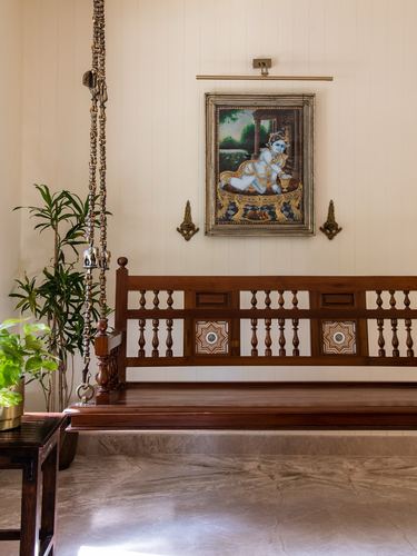 Wooden carved bench beneath a framed Krishna painting flanked by brass sconces in a foyer