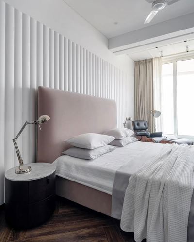 Blush pink upholstered bed against a white fluted wall in a minimalist bedroom