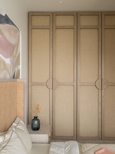 Wardrobe with cane-paneled wood doors and circular pulls beside a woven headboard and bed