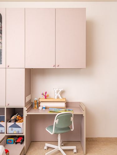 Child's study nook with pink cabinetry, built-in desk, and green swivel chair
